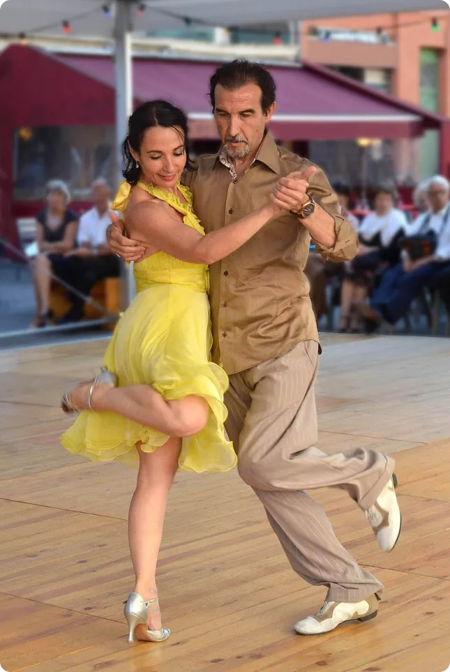 A man and woman gracefully engaged in a tango dance, surrounded by the lush greenery of a park.