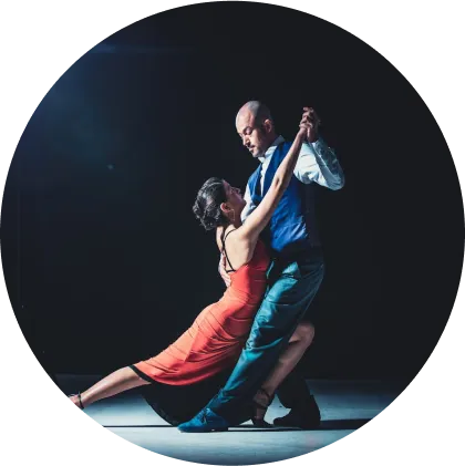 A couple joyfully dances in a circle, with the man positioned at the center, showcasing their connection and rhythm.