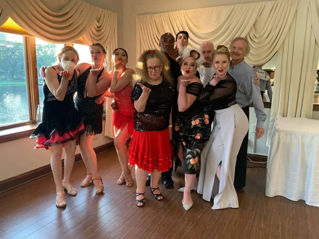 Group of adult dancers of all ages in sparkly Latin costumes blowing kisses together after a dance event, showing the social benefits of dancing for adults
