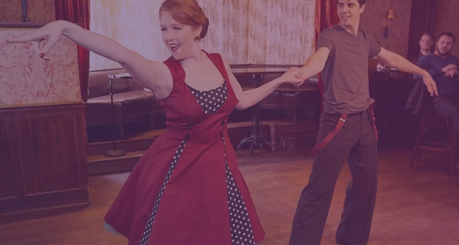 Couple dancing swing at a social dance venue while guests watch from a nearby table