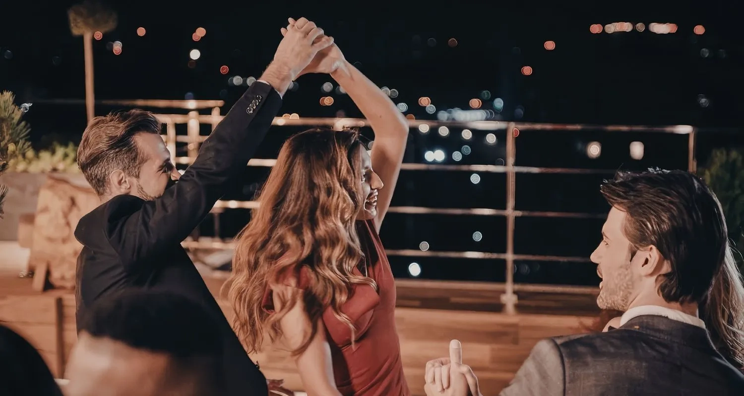 Couple social dancing on a rooftop terrace at night with city lights behind them