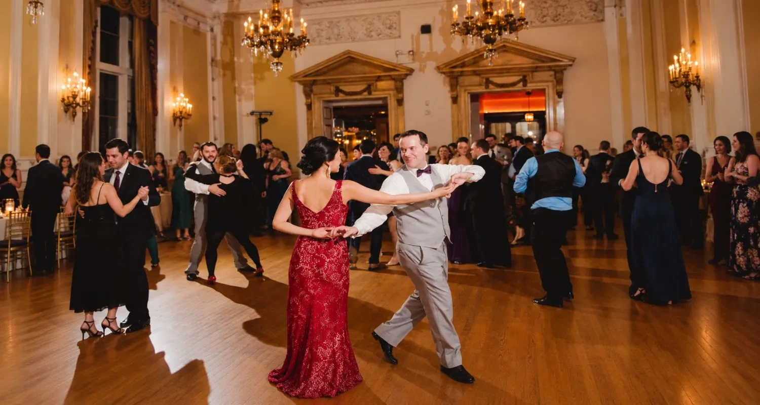 Couples social dancing at a crowded ballroom night in Philadelphia, PA under chandeliers