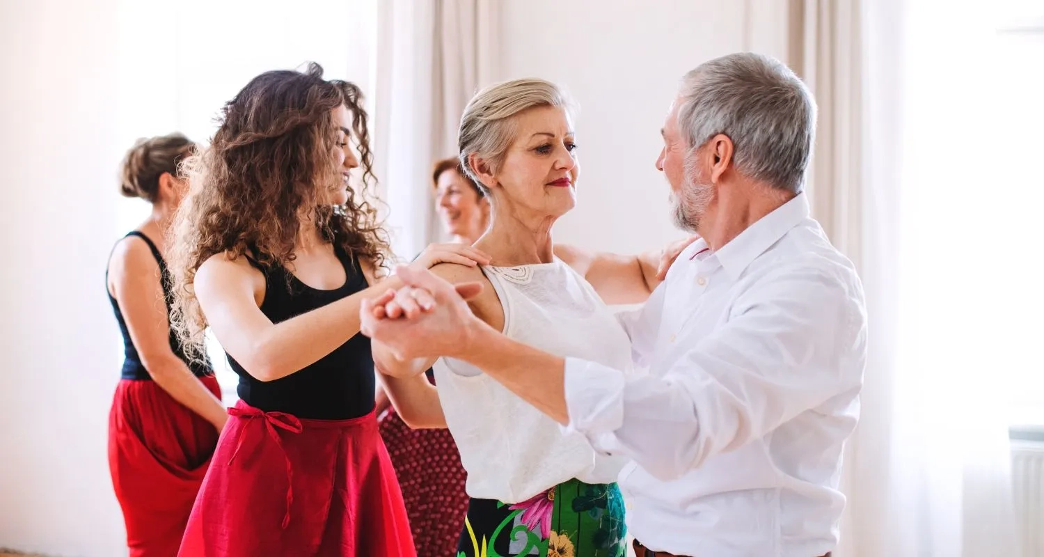 Beginners learning social dance in a group class, with an older couple in closed hold