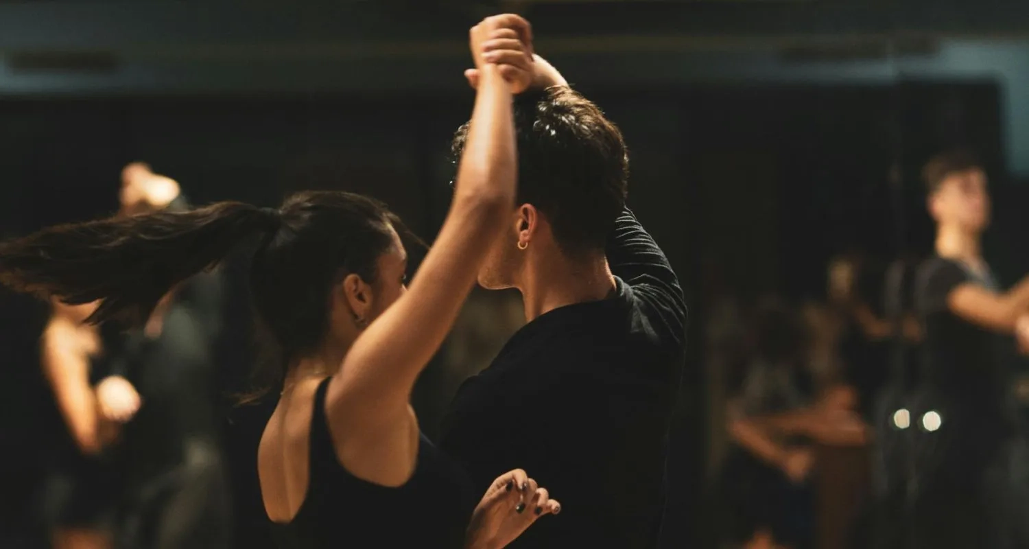 Couple mid-turn during a social dance, with other dancers reflected in the studio mirror