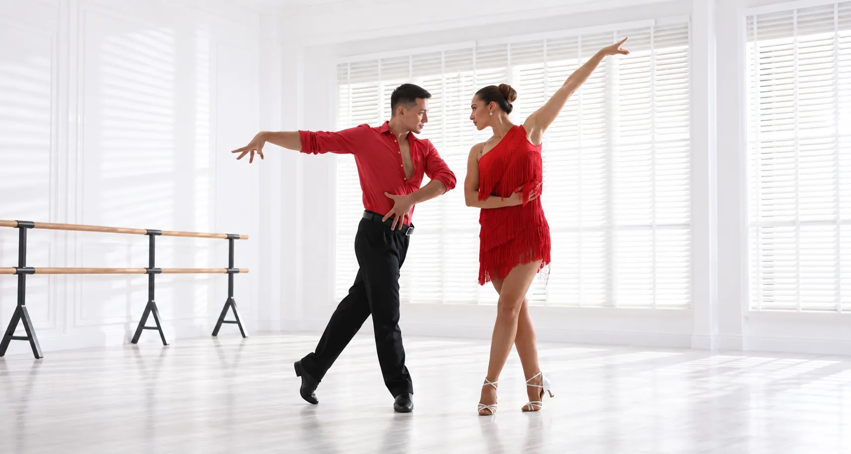 Couple practicing rumba dance in a bright dance studio with a mirror and barre